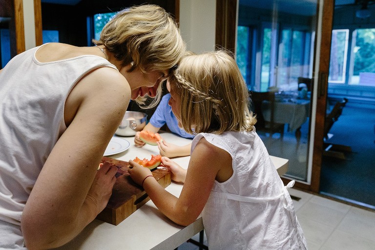 Mom and daughter touch heads and smile over eating watermelon.