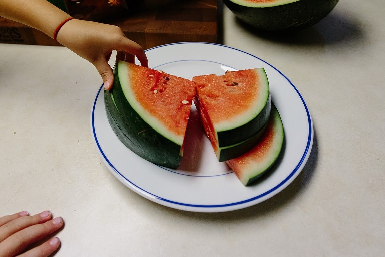A child's hand takes a watermelon slice from a white plate.