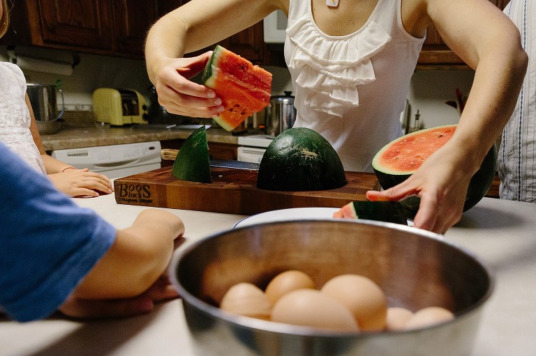 Mom puts triangle pieces of watermelon on a plate. Fresh brown eggs are in a bowl in the foreground. 