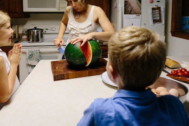 Mom slices the watermelon and is surprised. Daughter claps joyfully as the watermelon is split. 