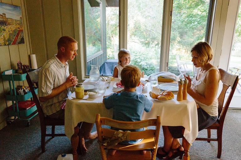 Four family members sit at the dinner table, hands clasped in prayer.