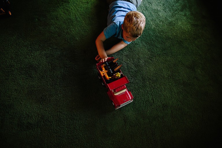Top down view of boy playing with red fire truck on green carpet. 