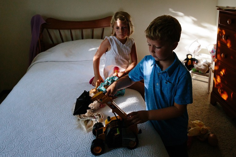 Dappled light on twins in a bedroom sharing a doll and a truck with each other. 