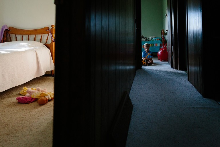 Camera left is warm bedroom and then long view down the hallway of boy playing with a toy crane. 