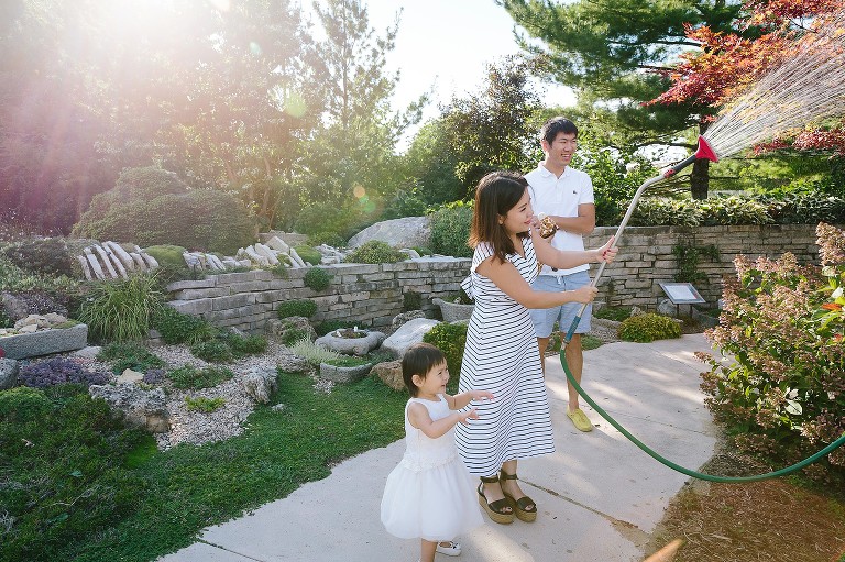 Family waters the garden with a hose and stream of water. Sun flare in the background 