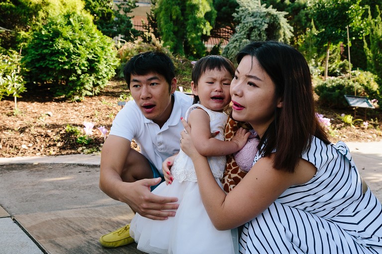 Two year old has tears while both parents comfort her 