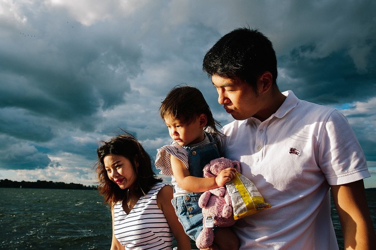 Family looks at ducks on lake. Dramatic clouds and light present