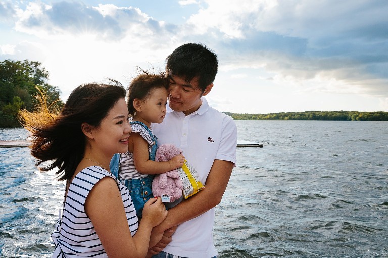 Family together on pier, hugging tight, blue skies, wind blowing hair