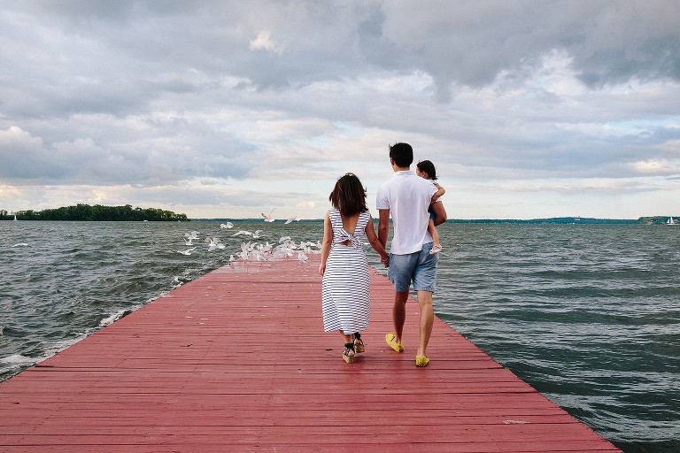 Family disrupts a red pier of seagulls as they walk toward the end of the dock. Stormy weather in sky