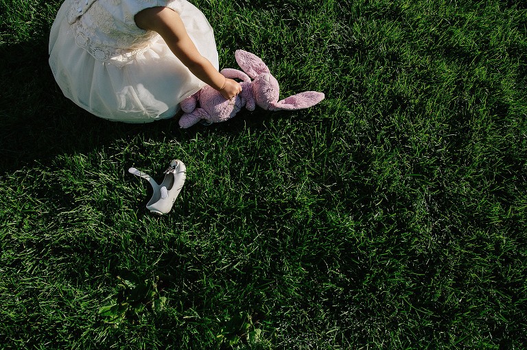 2 year old picks up pink bunny on green grass. 