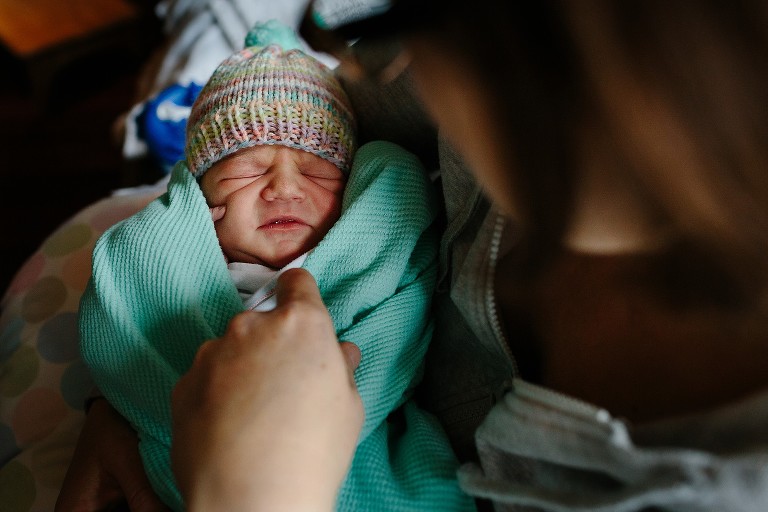 Mother pulls down blanket to reveal full face of distressed newborn 