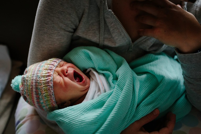 Newborn baby yawns in mother's arms 
