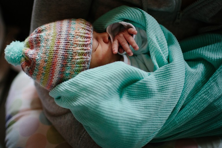 Swaddled newborn is sleeping in mom's arms. 