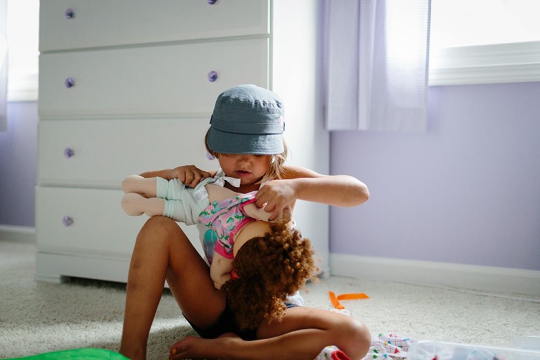 5 year old changes doll's clothes in her bedroom. 