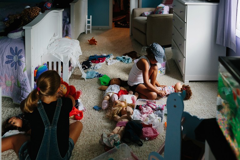 5 and 7 year old girls changes doll's clothes in her bedroom. 