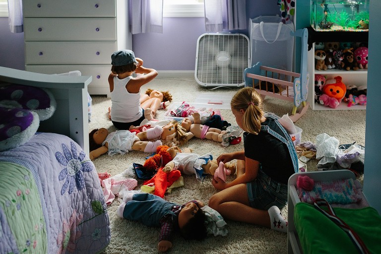 5 and 7 year old girls changes doll's clothes in her bedroom. 