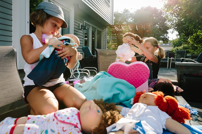 Sisters bring dolls outside to play. They pretend feed them and change their clothes. 