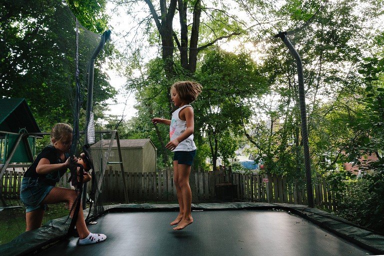 5 year old girl is jumping on trampoline while waiting for her 7 year old sister to join 