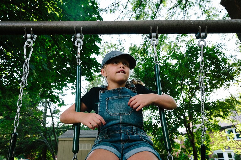 Girl looks out over backyard from swing set perch