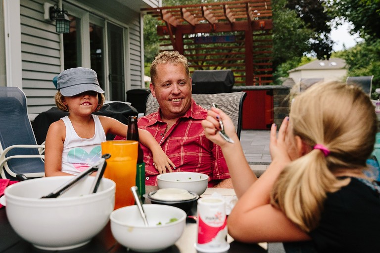 5 year old hugs dad. Dad is laughing and looking at 7 year old telling a joke to him.