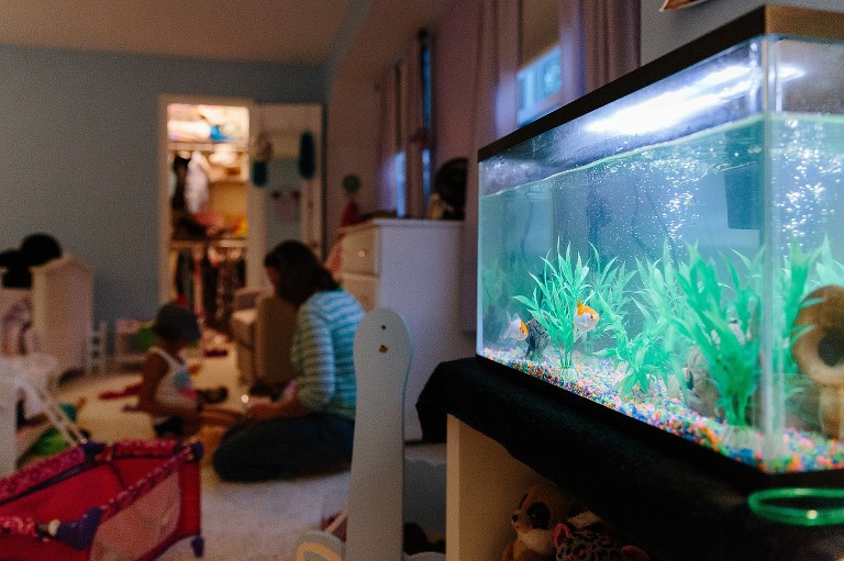 Focus on fish in tank while mother helps daughter in dark bedroom.