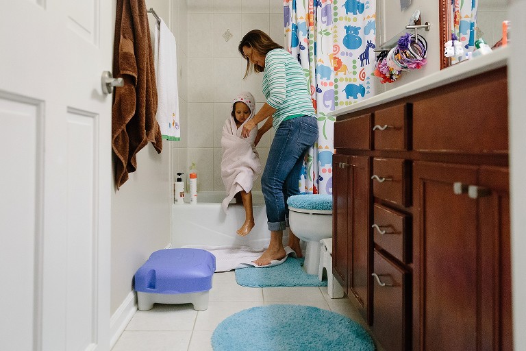 Mom helps daughter step out of shower in a towel. 