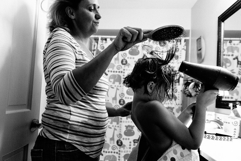 Mom brushes daughter's wet hair as she blow dries it with hair dyer. 