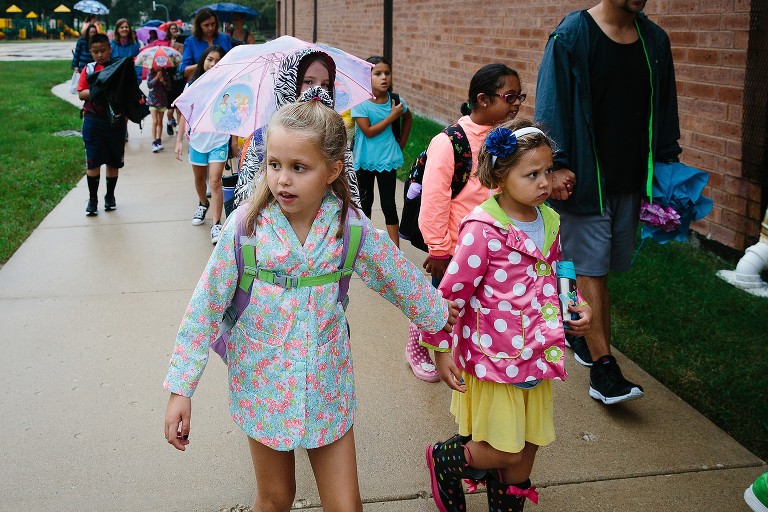 Big sister takes little sister's hand in crowded school path. 