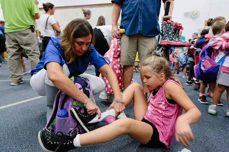 Mom helps daughter put on new shoes in a crowded gym