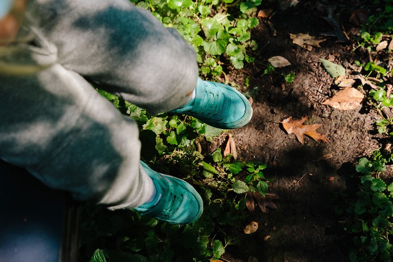 Dappled light exposes a fallen oak leaf. Girl's feet dangles on playground equipment over the leaf.