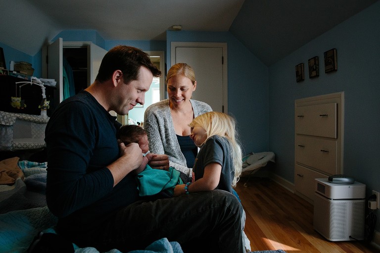 Daughter looks at newborn, Mom looks at newborn, Dad looks at daughter. Everyone smiling. 