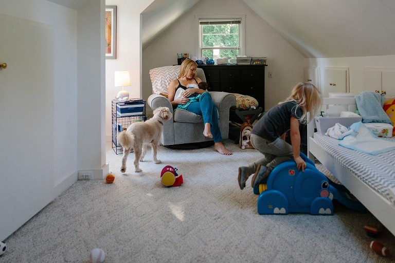 Daughter jumps on toy, dog looks at mom, mom looks at newborn while nursing 