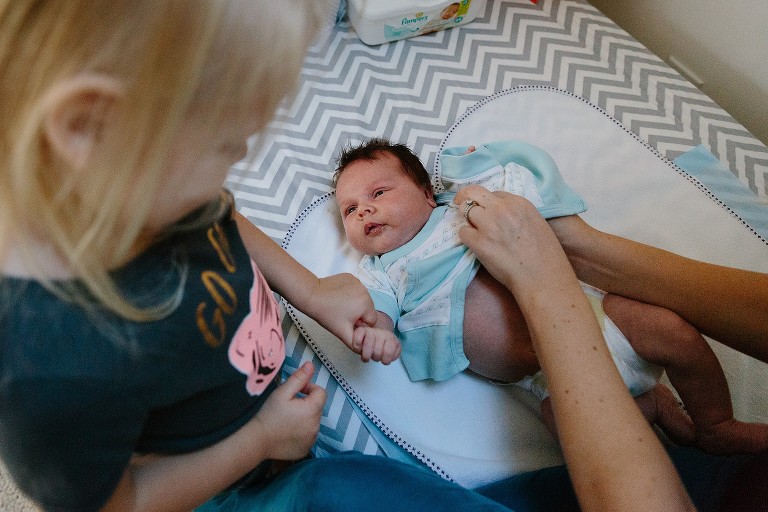 Sister holds baby brother's hand while getting changed. 