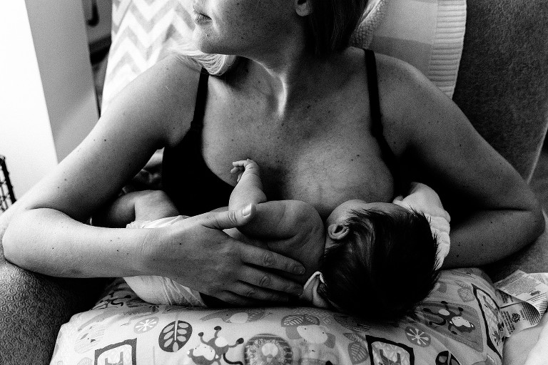 Mother nurses newborn in chair. 