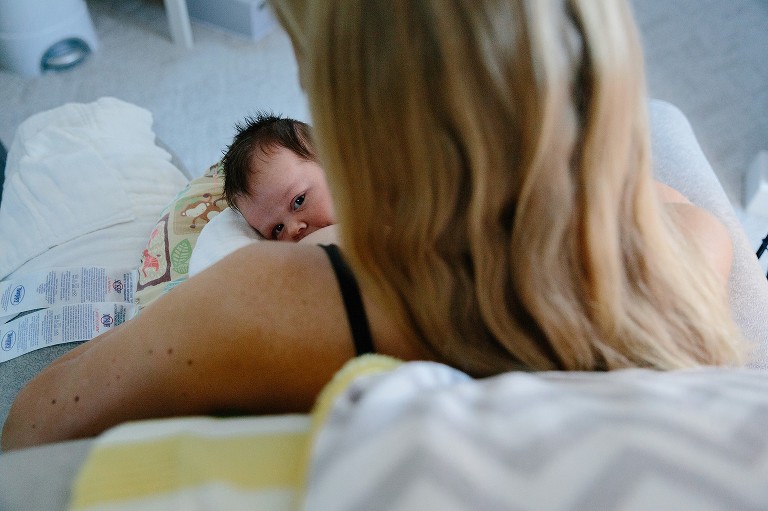 Mother nurses newborn in chair. 