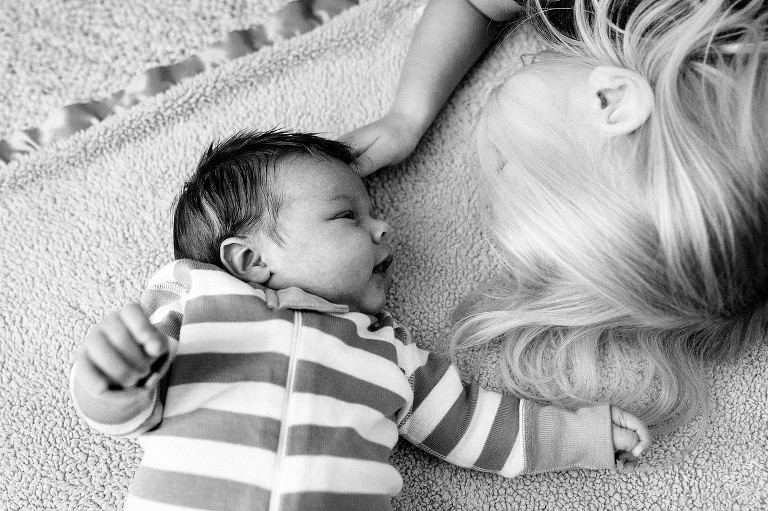 top down view of newborn son smiling and making eye contact with preschool sister