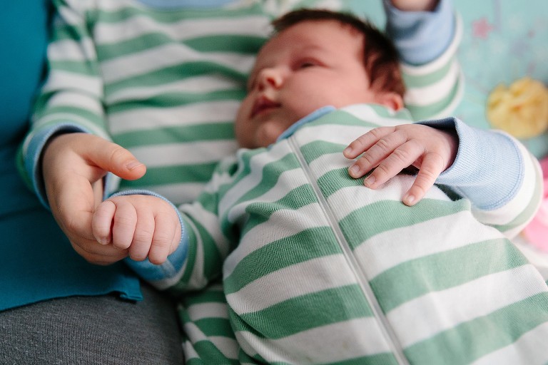 Preschooler holds new baby brother's hand. They are wearing matching green and white striped pajamas.