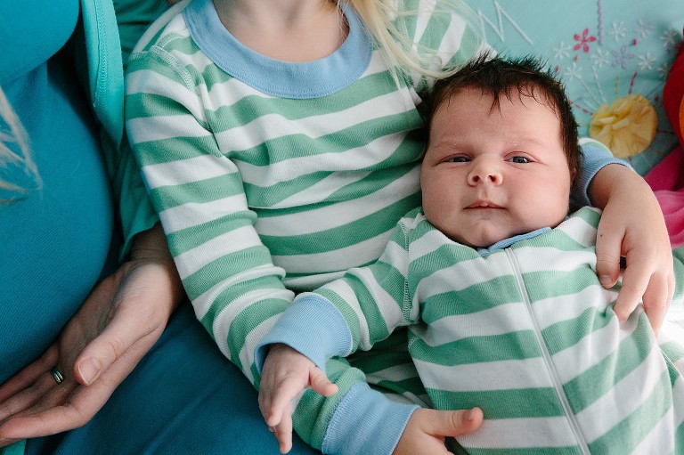 Preschooler holds new baby brother in lap. They are wearing matching green and white striped pajamas.