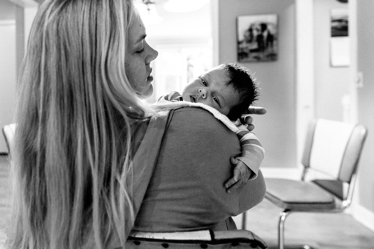 Mom holds newborn over shoulder, newborn is awake and making eye contact with camera