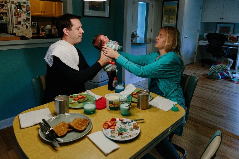 Mom passes newborn son to dad, breakfast on table 