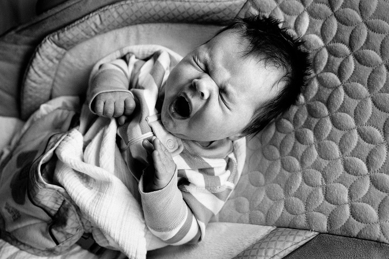 Black and white, newborn boy yawning wiht tightly closed eyes. 