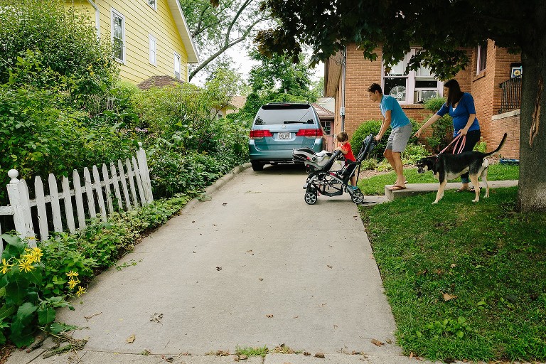 Family sets out for neighborhood walk with parents, son, newborn, and dog. 
