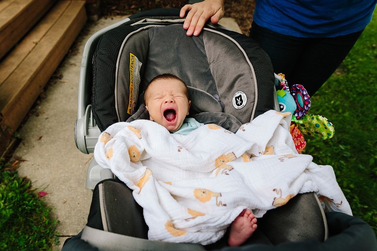 Newborn yawns in car seat.