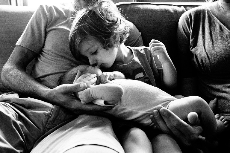 3 year old boy kisses the nose of newborn sister