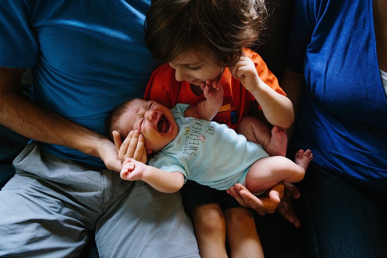 Top down view of preschool boy holding newborn sister, who is crying.