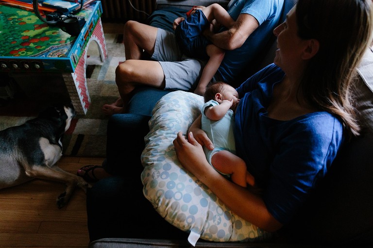 Mom nurses baby while preschool son is in similar body position, tickling, wiht dad. 