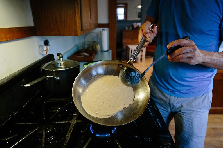 Dad tips crepe batter in pan.