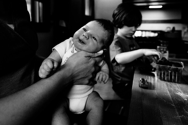 Portrait of newborn. Preschool son in the background, picking out raspberries.