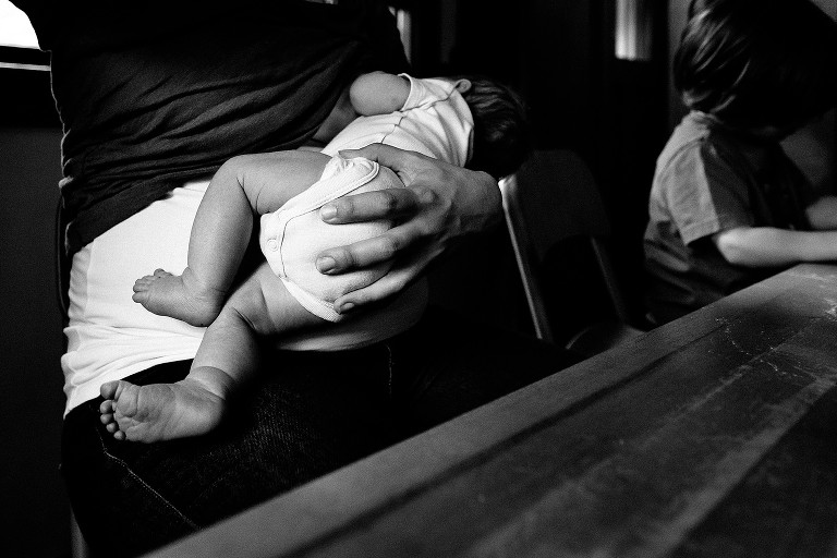 Focus on feet of nursing baby. Family seated at the table. 