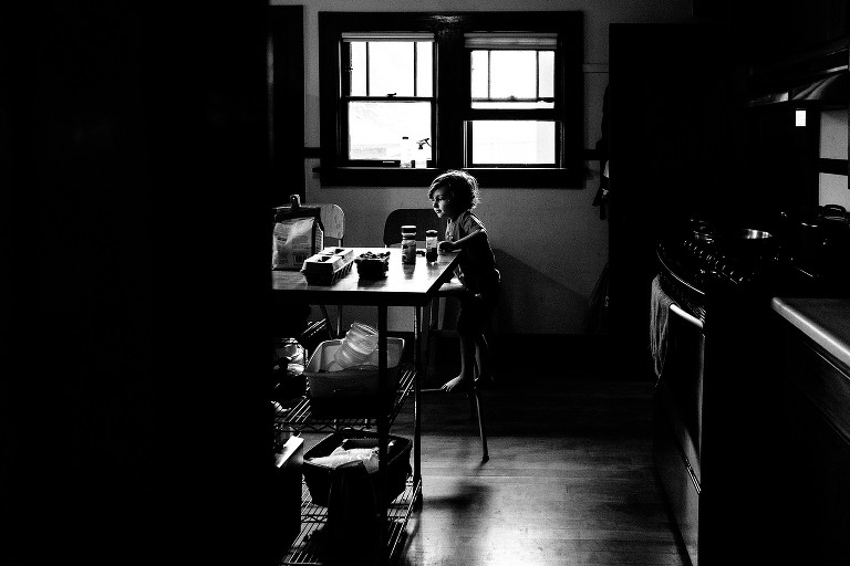 Black and white photo of boy alone in the kitchen. 